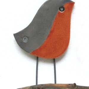 May include: A ceramic robin figurine with a gray back and orange belly, perched on a brown branch. The robin has black wire legs and two silver screws for eyes.