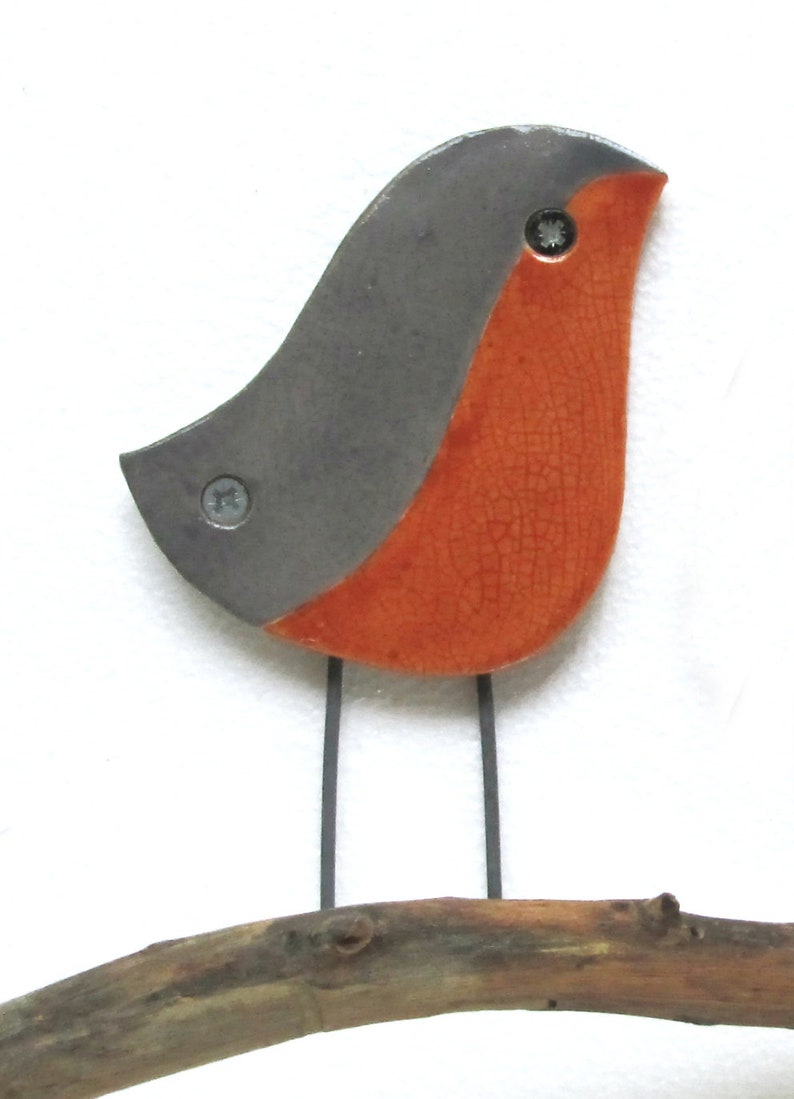 May include: A ceramic robin figurine with a gray back and orange belly, perched on a brown branch. The robin has black wire legs and two silver screws for eyes.