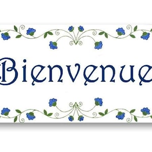 May include: White ceramic sign with blue floral border and the text "Bienvenue" in navy blue.