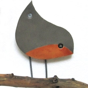 May include: A ceramic bird figurine with a gray body and an orange breast, perched on a brown branch. The bird has a simple, abstract design and is attached to the branch with metal screws.