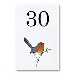 Pode incluir: Azulejo de cerâmica branco com o número 30 impresso em preto. Um pequeno pássaro cinza e laranja está empoleirado em um galho com folhas verdes.
