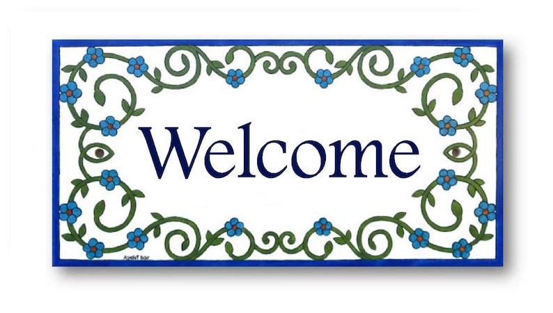 May include: A white ceramic tile with a blue border and a green floral design. The tile says "Welcome" in blue lettering.