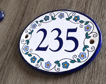 May include: White oval ceramic house number sign with blue and green floral border and the number 235 in blue.