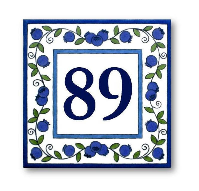May include: White ceramic tile with a blue border and a blue floral design. The number 89 is printed in blue in the center of the tile.