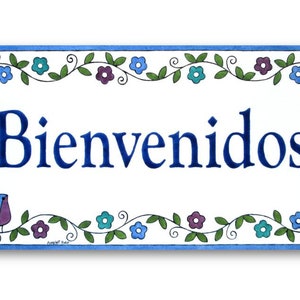 May include: A white ceramic sign with a blue border and floral design. The sign says "Bienvenidos" in blue lettering.