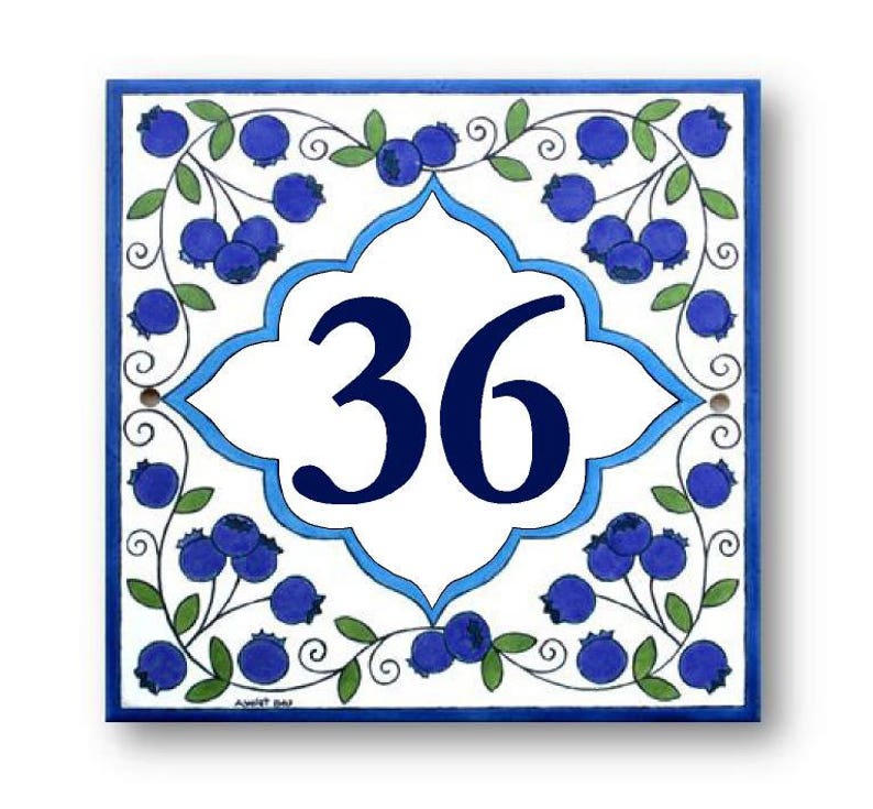 May include: A white ceramic tile with a blue and white border design. The tile features a blue floral pattern with blueberries and a white center with the number 36 in blue.