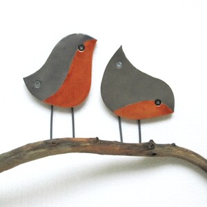 May include: Two ceramic birds with gray bodies and orange bellies perched on a brown branch. The birds are facing different directions.