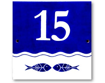 May include: Blue and white ceramic house number sign with the number 15 and two stylised fish below the number.