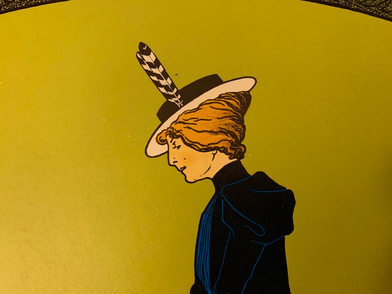 May include: A woman with blonde hair wearing a black hat with a white brim and a black and white feather. She is wearing a dark blue dress with a white collar.
