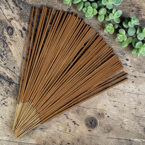May include: A collection of thin, brown incense sticks arranged in a fan shape. The sticks have a smooth, cylindrical body with a lighter, uncolored wooden base at the bottom end, fanned out to display the uniform texture and color of the incense.