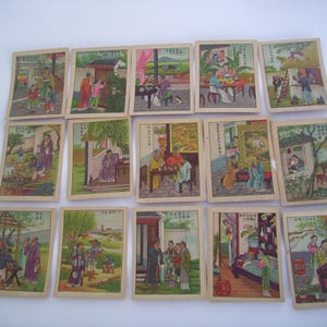 May include: A collection of fifteen vintage Chinese playing cards. Each card features a colorful illustration of people in traditional clothing, set against various outdoor and indoor scenes. The cards are arranged on a white surface.