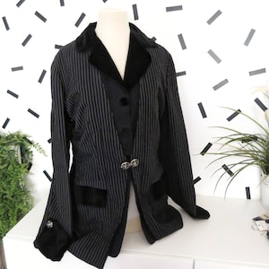 May include: A black and white striped blazer with a black velvet collar and cuffs. The blazer has a single button closure and two pockets.