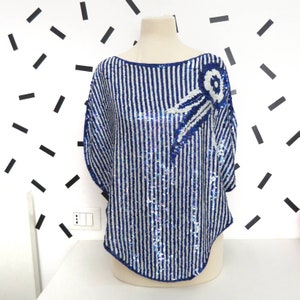 Puede incluir: Una blusa de lentejuelas azul y blanca a rayas con un diseño de lentejuelas azul y plata en la parte delantera.