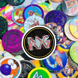 May include: A black and yellow circular patch with the word "POG" written in pink and blue letters on a black background. The patch is surrounded by a variety of colorful plastic game tokens.