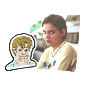 May include: An embroidered patch depicting a cartoon man with a distressed expression. The patch is on a white background next to a photograph of a young woman with a worried expression. The woman is wearing a light brown sweater with a diamond pattern.