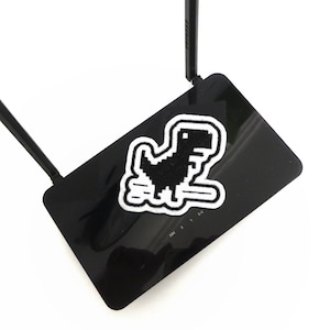 Pode incluir: Um roteador preto com um patch de dinossauro pixelado branco no topo. O roteador tem duas antenas.