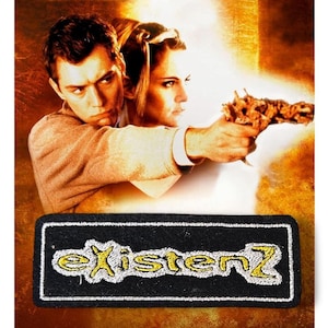 May include: A movie poster featuring two people, one holding a bio-mechanical gun. The poster has a warm color palette. The film title "eXistenZ" is embroidered on a black patch in yellow thread.