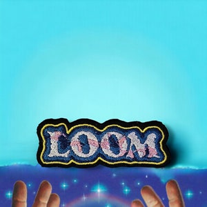 May include: A blue and pink embroidered patch with the word "LOOM" in a stylised font. The patch has a black border and is surrounded by a blue background.
