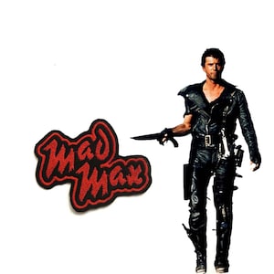 May include: Red embroidered patch with the words "Mad Max" in black outline. A man in a black leather jacket and trousers is holding a weapon.