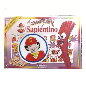 May include: A red and white talking pen with the words "La Penna Parlante di Sapientino" and "Molto Bene!" on the box. The box also features a cartoon character with a red hat and a blue shirt.