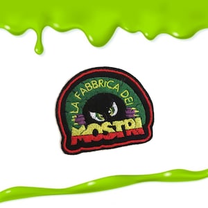 May include: A black and red embroidered patch with a cartoon monster face and the text "La Fabbrica Del Mostro" in a circle.