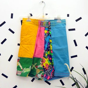 Puede incluir: Una falda de patchwork colorida con un patrón geométrico amarillo, rosa, azul, verde y negro. La falda tiene una cintura con la palabra "DEF" impresa.