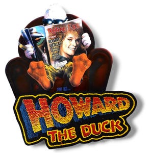 Pode incluir: Um remendo bordado preto com as palavras "Howard the Duck" em letras amarelas, vermelhas e azuis. O remendo apresenta uma imagem de desenho animado de Howard the Duck sentado em uma cadeira lendo uma revista.