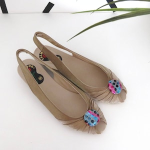 Puede incluir: Un par de zapatos de color dorado con puntera abierta y tira en el tobillo, con un botón de lunares de colores en cada zapato.