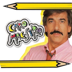 以下が含まれることがあります： カラフルな文字で「Caro Maestro」と書かれた白い刺繍パッチ。パッチは黄色と白のラインの背景にあり、鉛筆で縁取りされています。