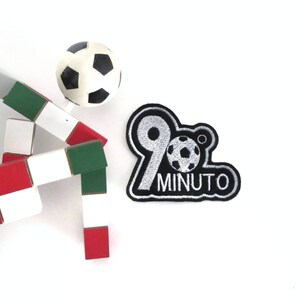May include: Black and white embroidered patch with a silver 90 and a football, with the text "MINUTO" below.