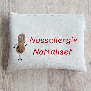 May include: A white zippered pouch with the words "Nussallergie Notfallset" in red, along with a cartoon peanut character. The pouch is designed to hold emergency supplies for those with nut allergies.