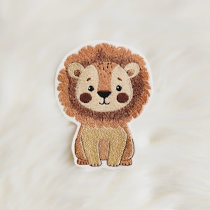 Könnte beinhalten: Gestickter Bügel-Patch mit einem Cartoon-Löwen mit brauner Mähne und hellbraunem Körper. Der Löwe sitzt mit seinen Pfoten vor sich und hat einen freundlichen Ausdruck.