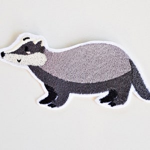 Könnte beinhalten: Gestickter Bügelaufkleber mit einem grauen und schwarzen Dachs mit weißem Gesicht.