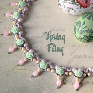 May include: A delicate necklace with pastel green and purple flowers and beads. The necklace has a pink and white color scheme and is called "Spring Fling".