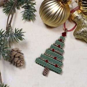 Puede incluir: Un adorno de árbol de Navidad de cuentas verdes con cuentas rojas y detalles dorados. El adorno está colgado de una cinta roja.