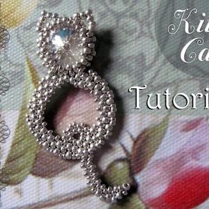 May include: A silver beaded cat figurine with a large clear rhinestone for a head. The cat is sitting on a floral patterned fabric. The text "Kitty Cat Tutorial" is visible in the background.