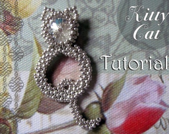 May include: A silver beaded cat figurine with a large clear rhinestone for a head. The cat is sitting on a floral patterned fabric. The text "Kitty Cat Tutorial" is visible in the background.