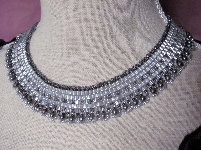 May include: A silver and gray beaded choker necklace with a graduated design. The necklace is made with small, round beads and larger, rectangular beads.