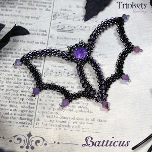 May include: A beaded bat-shaped necklace in black and purple. The necklace features a central purple gem and square purple accents. The word "Batticus" is written at the bottom, with "Trinkets beading" at the top.