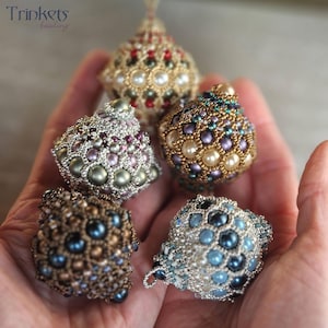 May include: Five beaded ornaments in various colors and patterns, including gold, silver, blue, green, and red. The ornaments are made with small beads and pearls, and they have a delicate, intricate design.