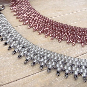 May include: Two beaded necklaces, one silver and one pink, with a fringe detail. The necklaces are made of small, square beads and are arranged in a graduated pattern.