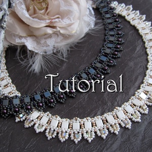 May include: Two beaded necklaces, one black and one white, with a square bead design. The necklaces are on a dark background with a white flower and feathers.