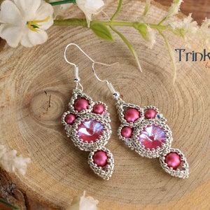 Op de afbeelding: Een paar zilveren oorhangers met roze en heldere kralen. De oorbellen hebben een traanvorm met een grotere kristallen kraal in het midden.