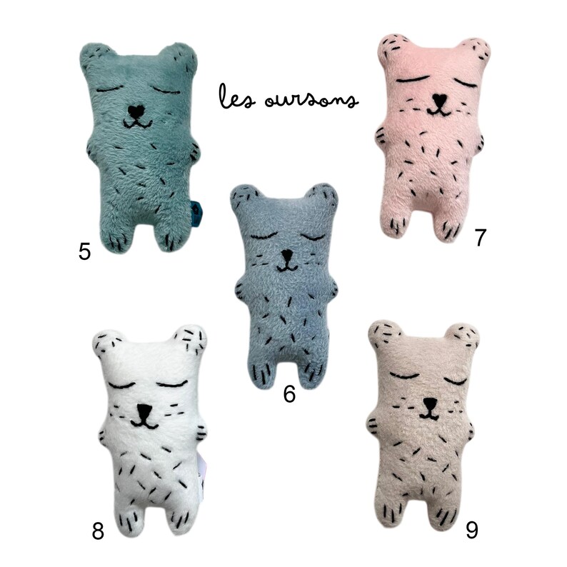 May include: Five plush bear toys in various colors: teal, pink, blue, white, and beige. Each bear has closed eyes, a black stitched nose, and black stitched details. The text "les oursons" is written in black cursive.