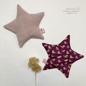 May include: Two star-shaped pillows, one pink with gold embroidery and the other burgundy with a bird pattern. The text "UNE ÉTOILE DANS MA CABANE. play love music" is visible in the top right corner of the image.
