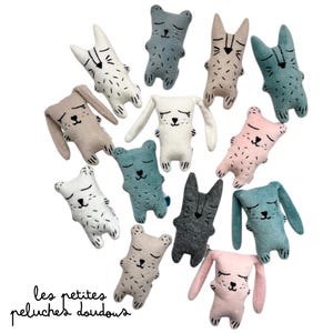 May include: A collection of plush animal toys in various colors, including white, gray, pink, and teal. The toys feature closed eyes and stitched details, with some resembling bears and others rabbits. The text "les petites peluches doudous" is at the bottom.