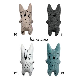 May include: Four plush bunny toys in beige, gray, white, and teal. Each has a minimalist face design with closed eyes and a small nose. The toys are labeled with numbers 10, 11, 12, and 13. The text "les renards" is written below the toys.