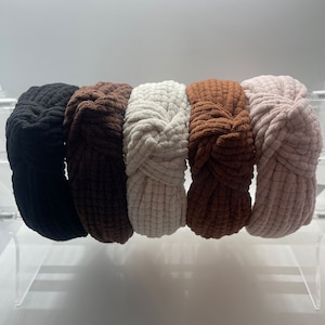 May include: Five knotted headbands in different colors: black, brown, white, brown, and pink. The headbands are made of a soft, textured fabric.