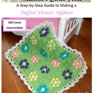 Könnte beinhalten: Ein Häkelmuster für eine grüne, gepuffte Blumen-Decke, die für 45,7 cm große Puppen entworfen wurde. Die Decke hat einen weißen Häkelrand und ist mit bunten Blumen verziert.