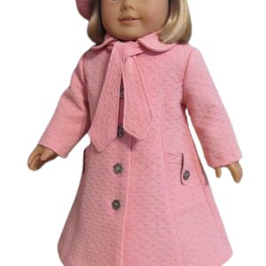 Puede incluir: Un abrigo rosa para mu&ntilde;eca con un gorro a juego y un lazo. El abrigo tiene una corbata en el cuello y botones en la parte delantera. La mu&ntilde;eca lleva zapatos blancos.